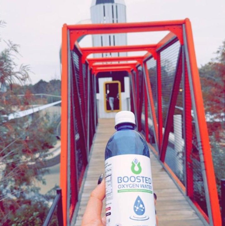 Hand holding a Boosted bottle on a red footbridge
